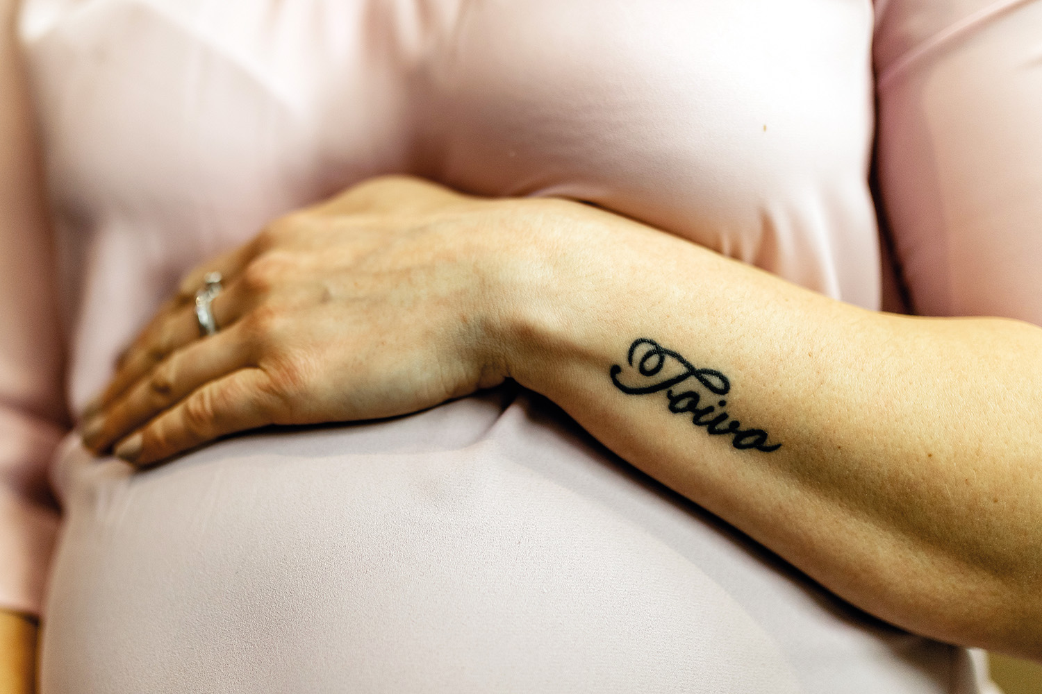Hand på gravid mage. I handleden finns texten Toivo tatuerad.